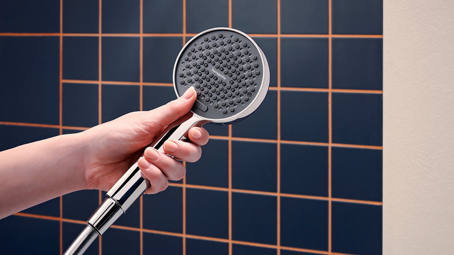 Chromowana słuchawka prysznicowa na tle granatowej płytki fot. Hansgrohe
